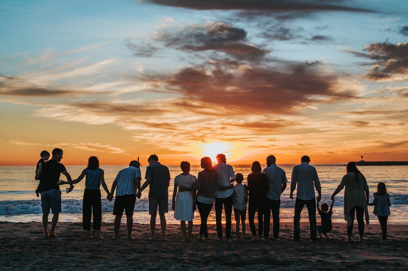 A multigenerational family holding hands on a beach at sunset